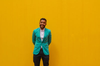 Portrait of smiling young man standing against yellow wall