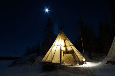 Tent on snow covered land against sky at night