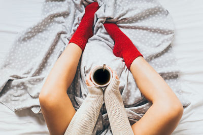 Low section of woman holding black coffee on bed