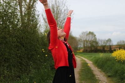 Smiling woman standing with arms raised against plants