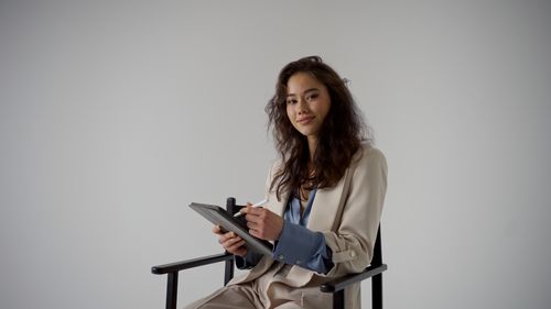 Young woman using mobile phone while standing against wall