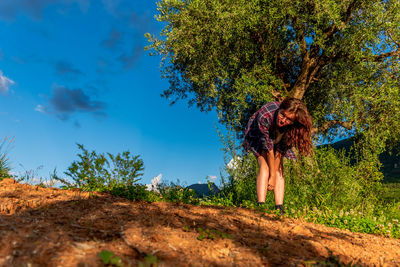 Woman standing by tree on field against blue sky