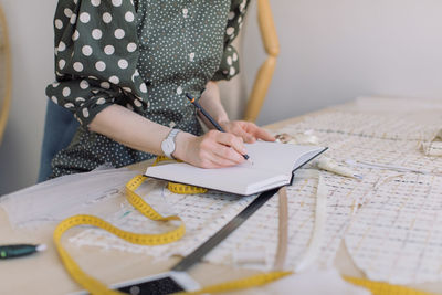 Midsection of woman writing in book at table