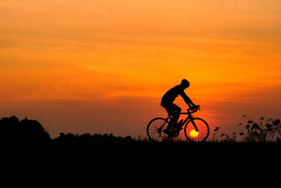 Silhouette of man riding bicycle against sunset sky