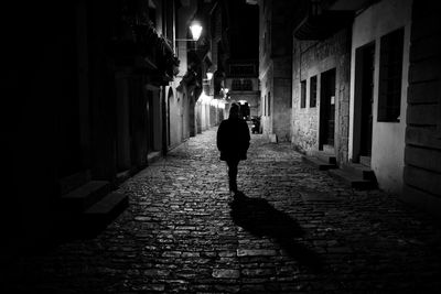 Rear view of man walking on street amidst buildings at night