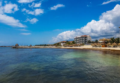 View of buildings by sea against cloudy sky