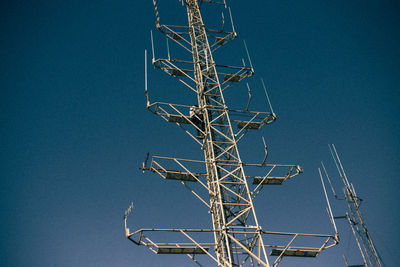 Low angle view of electricity pylon against clear blue sky