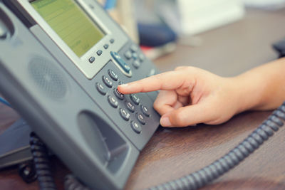 Cropped hand of person dialing telephone keypad on table