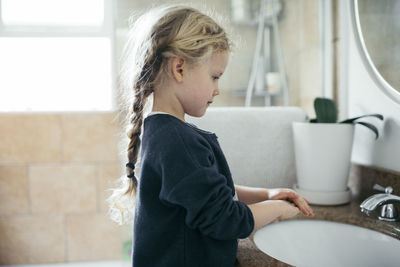 Side view of girl washing hands at sink in bathroom