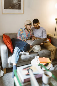 Gay couple using laptop while sitting on sofa at home