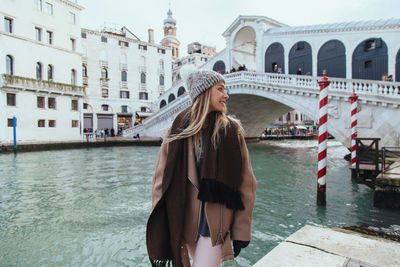 Smiling young woman standing by canal in city