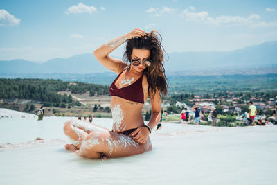 Young woman wearing bikini while sitting on sand at beach