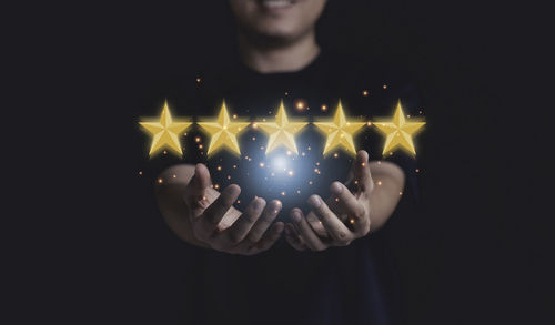 Midsection of man holding illuminated ball against black background