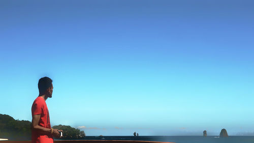 Man standing by sea against clear blue sky
