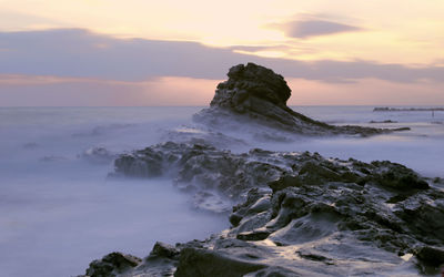 Scenic view of rocks on shore against sky during sunset