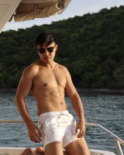 Portrait of shirtless man wearing sunglasses sitting on the yacht during sunset 