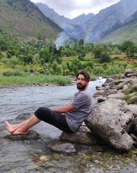 Young man sitting on rock against mountains