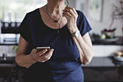 Midsection of senior woman holding smart phone in kitchen at home