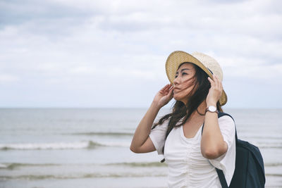 Beautiful woman wearing hat looking away while standing on beach