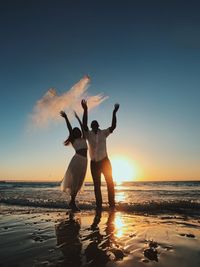 Friends standing on beach against sky during sunset