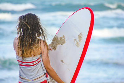 Rear view of woman standing with surfboard by sea