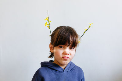 Portrait of funny little girl with flowers on top of the head making angry face