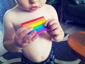 Close-up of shirtless baby boy holding multi colored toy at home