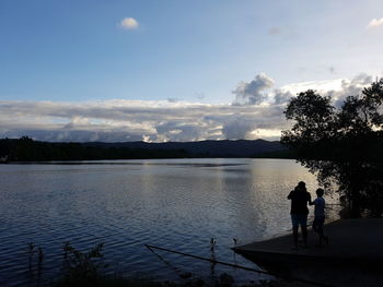 Silhouette of people standing by lake against sky