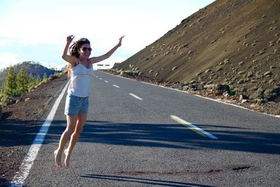 Full length of cheerful woman jumping with arms raised on road