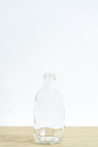 Close-up of empty glass bottle on table against white background