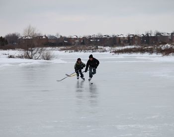 Friends playing ice hockey on rink against sky