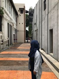 Rear view of man walking on footpath amidst buildings