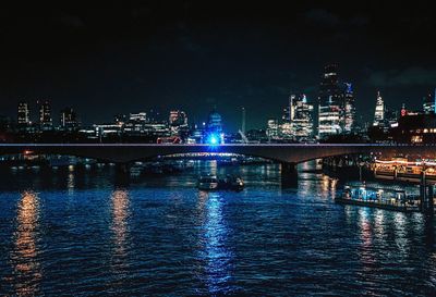 Illuminated bridge over river by buildings against sky at night