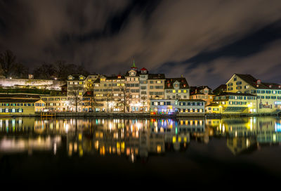 Illuminated cityscape by river against sky at night