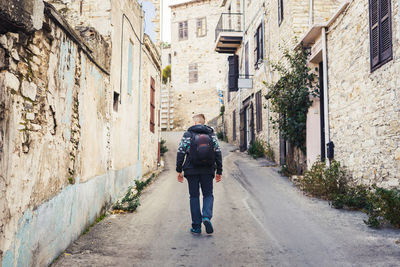 Rear view of man walking on footpath amidst buildings