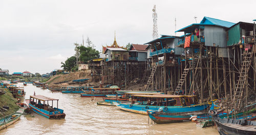 Boats moored at port by buildings against sky