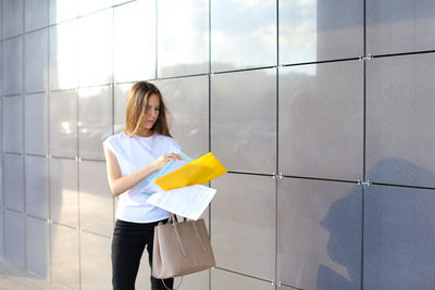 Businesswoman reading document while standing against wall
