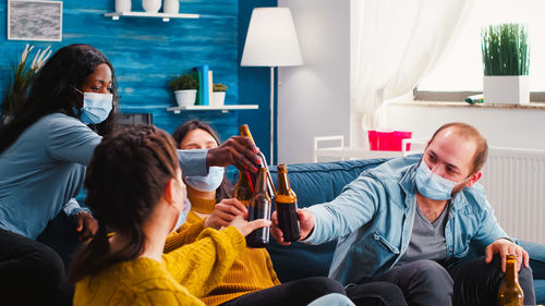 Friends toasting beer bottles while sitting at home