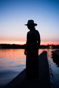 Silhouette girl standing in boat on lake against sky during sunset