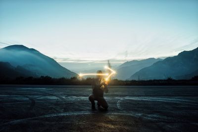 Man with arrow symbol light painting against mountains during sunset