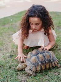 Girl touching turtle while crouching on field