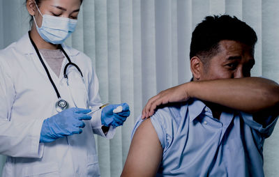 Young doctor wearing mask vaccinating patient in clinic