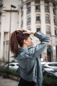 Side view of woman with hand in hair standing in city