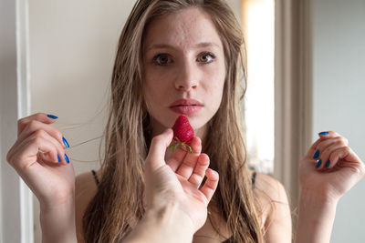 Cropped hand of woman feeding strawberry to friend at home