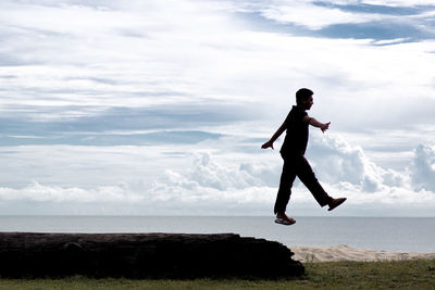 Man jumping from retaining wall against sea and sky