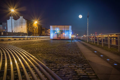 Illuminated street lights by bridge against sky at night