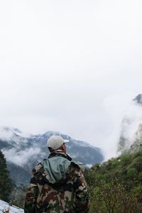 Rear view of man looking at mountains against sky