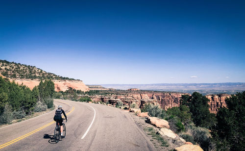 Rear view of man riding bicycle on road against clear blue sky