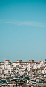 Sailboats in city by buildings against blue sky