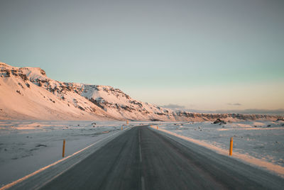 Road amidst snow covered land against sky at sunset